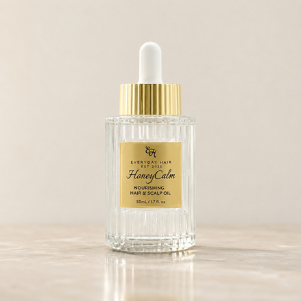 Bottle of 'HoneyCalm' nourishing hair and scalp oil with a dropper on a beige background