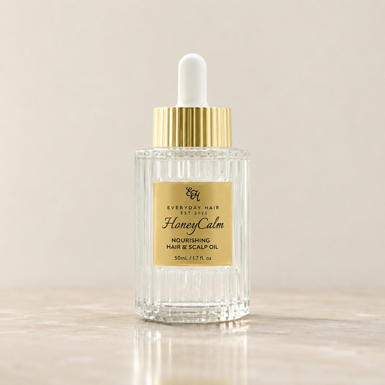 Bottle of 'HoneyCalm' nourishing hair and scalp oil with a dropper on a beige background