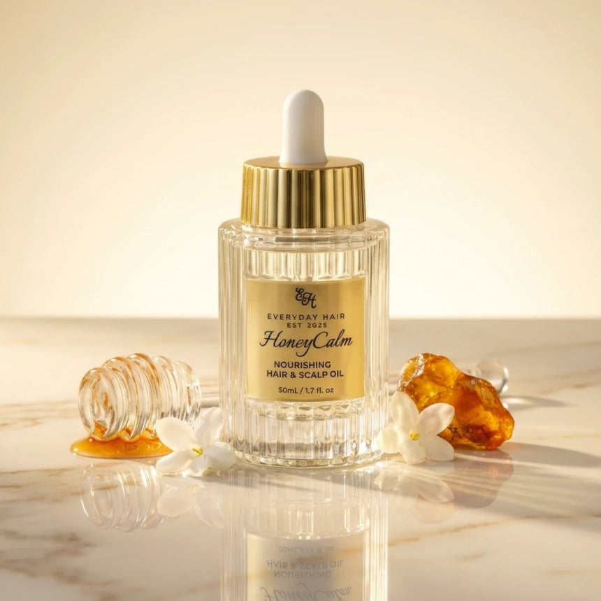 Bottle of HoneyCalm nourishing hair and scalp oil with dropper, placed on a marble surface with honey and flowers.