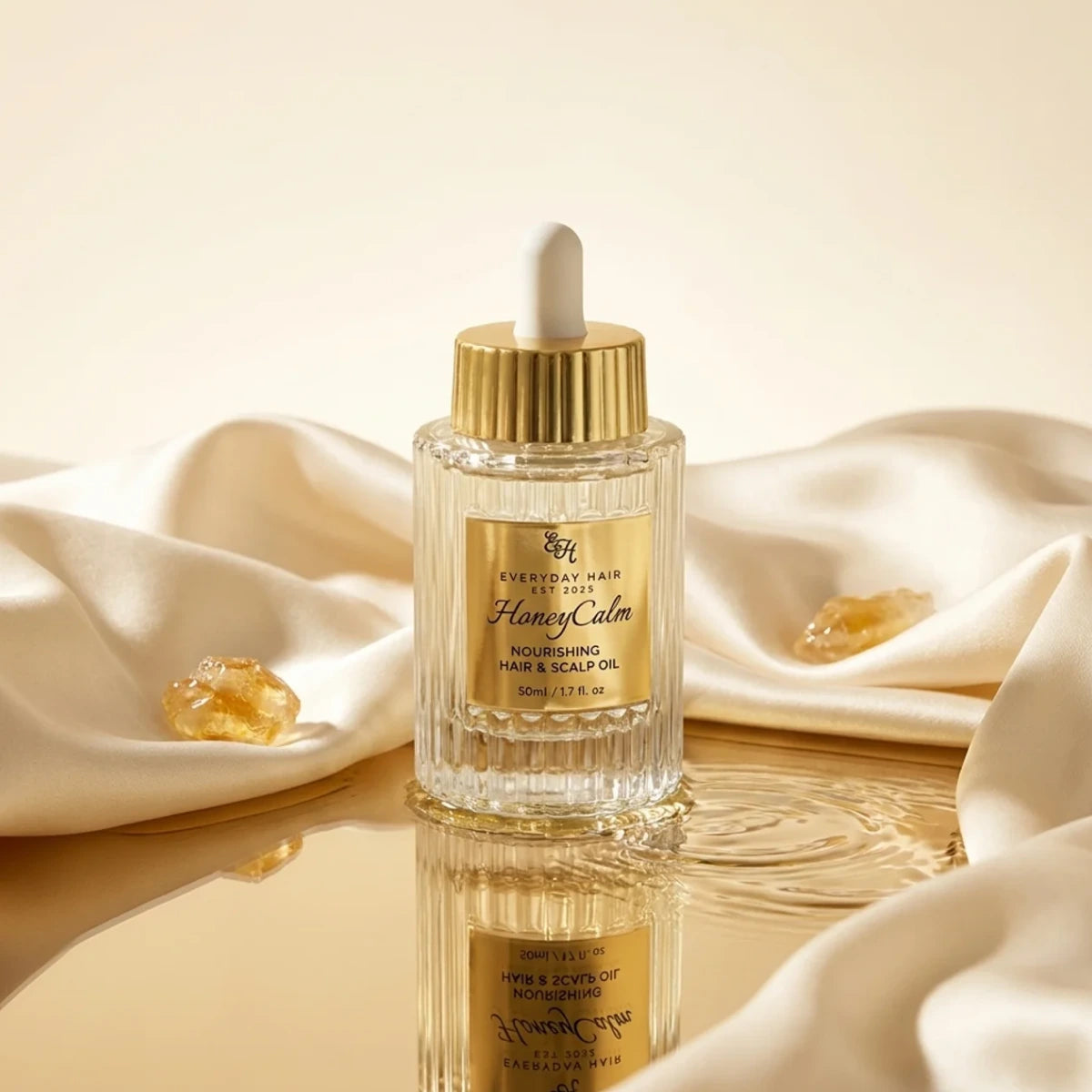 Bottle of HoneyCalm nourishing hair and scalp oil with dropper on silk fabric with golden reflections.